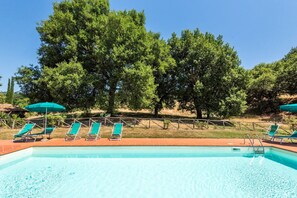A swimming pool with lounge chairs and umbrellas, surrounded by trees.