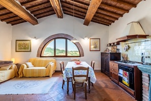 Una cocina rústica con un arco de piedra en la ventana, vigas de madera en el techo, una mesa de comedor con sillas y una encimera.