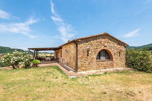 Un edificio de piedra con un patio cubierto, rodeado de vegetación y colinas.