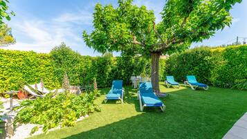 Un jardin avec un arbre, une pelouse verdoyante et des chaises longues bleues.