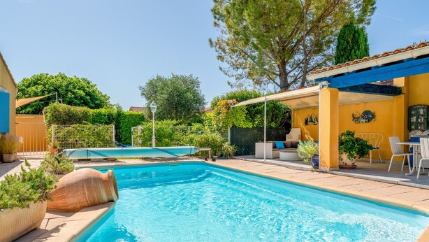 Una piscina con ombrellone, circondata da piante in vaso e una zona patio con mobili da esterno.