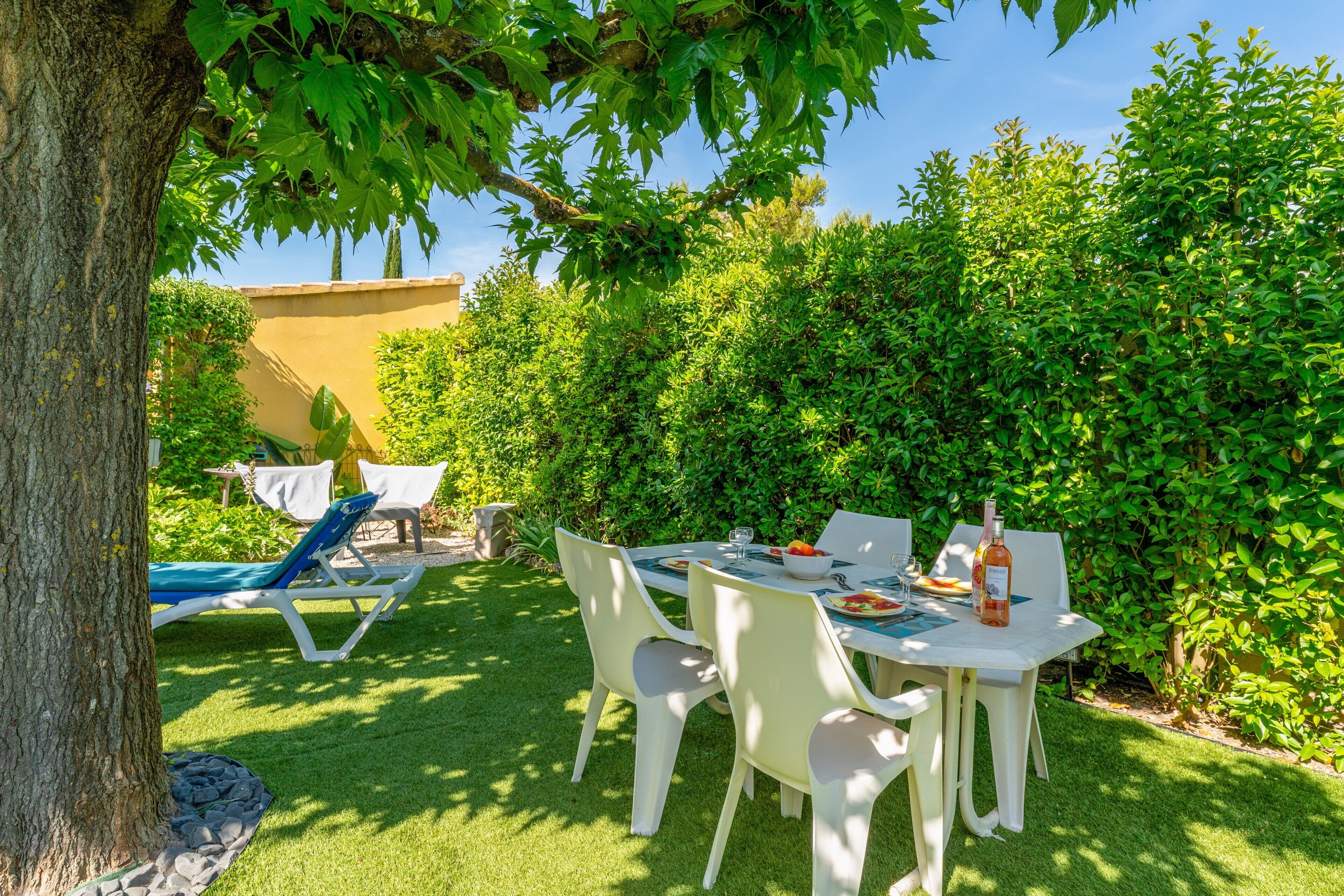 An outdoor patio with a table, chairs, and a bottle of wine.