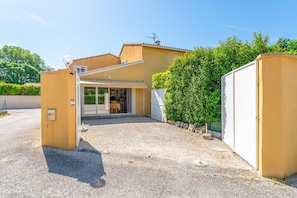 A residential property with a covered patio, a gravel driveway, and a white gate.