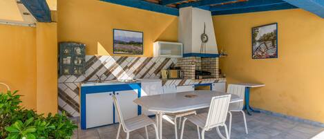 An outdoor kitchen area with a tiled floor, a white table with chairs, and a brick oven.