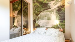 A bedroom with a bed, a mirror, a wall-mounted lamp, and a waterfall mural. - Holiday Home “L'Olivier” with Shared Pool, Wi-Fi & Air Conditioning (L'Isle-sur-la-Sorgue)