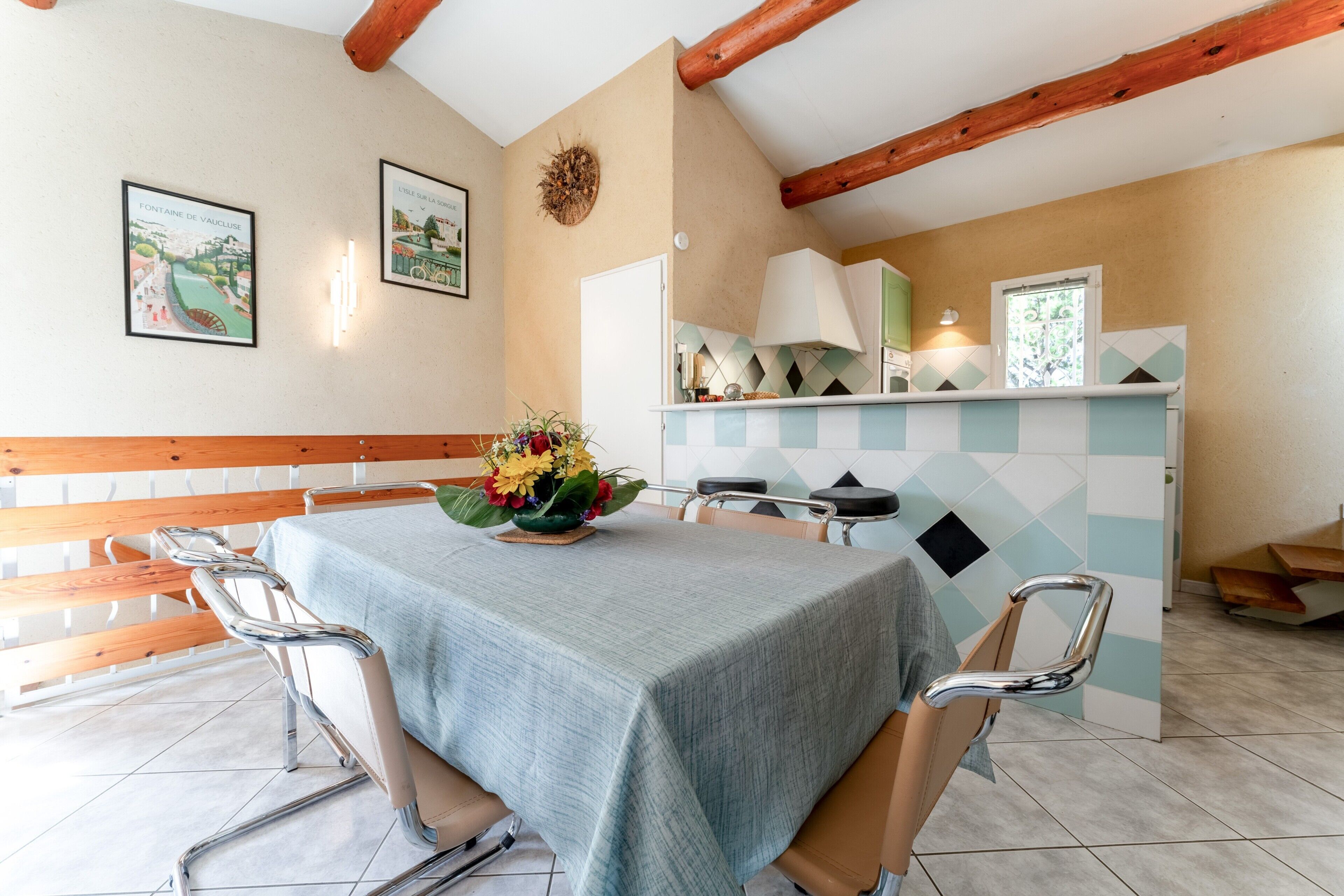 A dining area with a table set for four, a bench, and a kitchen area with a tiled backsplash.