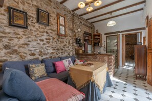 Un intérieur rustique avec un mur en pierre, un plafond en bois, un canapé avec des coussins, une petite table et un coin cuisine équipé d’un four à micro-ondes et de placards.