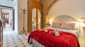 Een slaapkamer met een groot bed, een houten garderobe, een kapstok en een stenen boog.