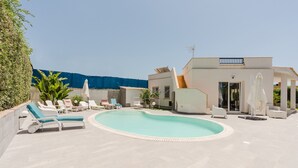 A modern outdoor pool area with lounge chairs, a covered seating area, and a building with a staircase.