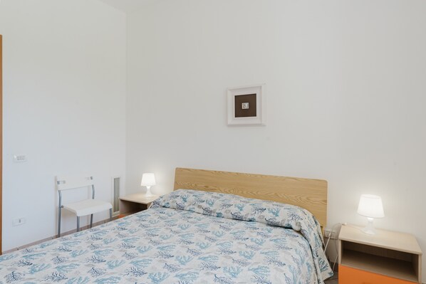 A bedroom with a bed, two bedside tables, a chair, and a wall-mounted picture.