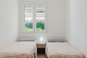 A bedroom with two beds, a nightstand with a lamp, and a window with shutters.