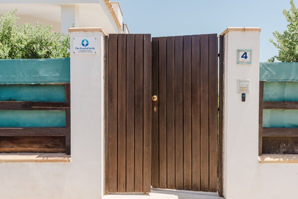 A gated entrance with a wooden door, a sign indicating 'The Pearl of Sicily,' and a number '4' on a wall.
