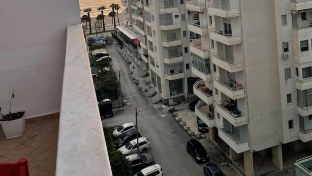 A high-rise residential building with multiple balconies, a parking area, and a view of the sea at sunset. - Spacious Sea View Apartment Private Balcony · Steps to Beach · Vlora Albania (Vlore)
