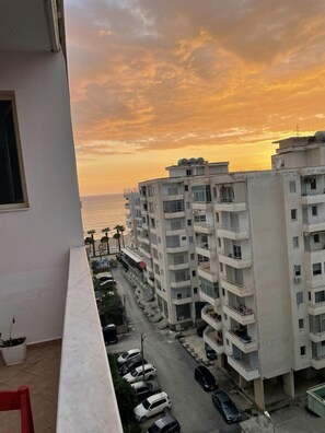 Ein Hochhaus mit mehreren Balkonen, einem Parkplatz und Blick auf das Meer bei Sonnenuntergang.