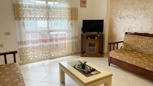 A living room with a sofa, a coffee table, a TV on a stand, and a window with curtains. - Spacious Sea View Apartment Private Balcony · Steps to Beach · Vlora Albania (Vlore)