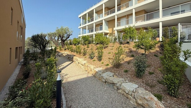 A multi-story building with balconies, a gravel pathway, and a landscaped area with shrubs and trees. - Modern studio - terrace - pool (Villeneuve-Loubet)