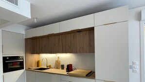 A modern kitchen with white cabinetry, a wooden countertop, and a built-in oven. - Modern studio - terrace - pool (Villeneuve-Loubet)