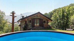 A stone house with a wooden door, a swimming pool in the foreground, and a mountainous backdrop. - Deluxe Room "Chalet Cuore Selvatico" with Mountain View, Terrace, and Private Garden (Monno)