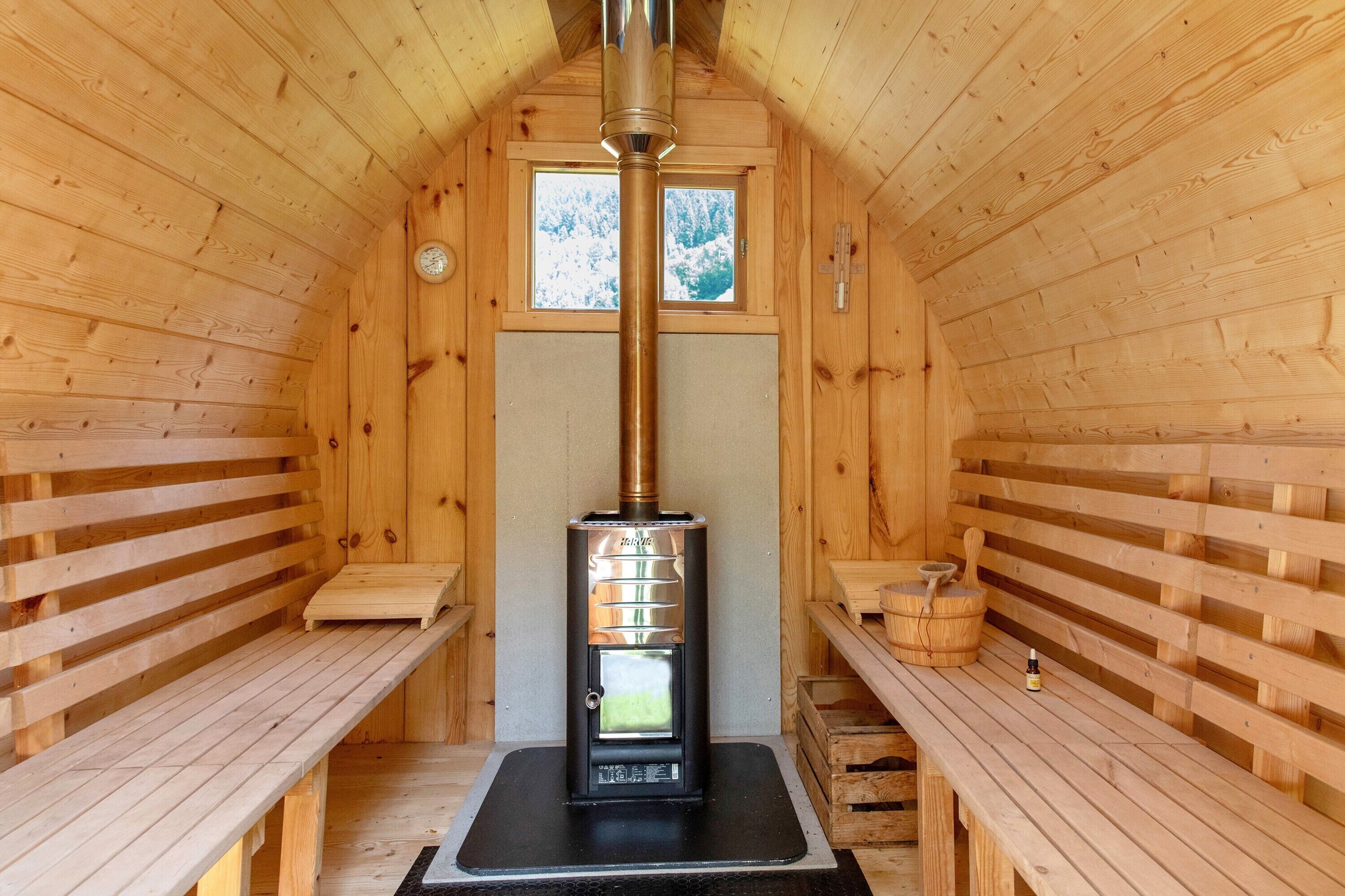 Un sauna de madera con bancos, un equipo de sauna y una ventana con vistas nevadas.