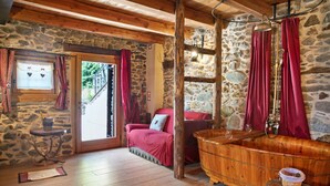A stone-walled room with a wooden bathtub, a red chair, and a small table with a basket. - Deluxe Room "Chalet Cuore Selvatico" with Mountain View, Terrace, and Private Garden (Monno)