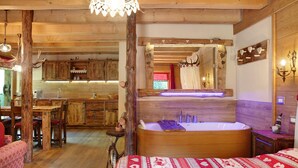 Un intérieur en bois comprenant un grand lit, une baignoire en bois, un coin repas et une cuisine.