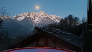 Un bain à remous avec vue sur les montagnes, un bâtiment en pierre et un ciel dégagé.