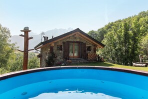 A stone house with a wooden door, a swimming pool in the foreground, and a mountainous backdrop. - Apartment in Chalet 'Open Space Deluxe' with Mountain View and Private Garden (Monno)