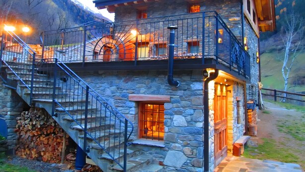A stone building with a balcony, a staircase, and a chimney.