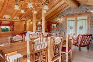 Un interior de madera con techo alto, paredes de piedra y un comedor con mobiliario de madera.