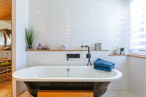 Un bagno moderno con una vasca freestanding, pareti piastrellate di bianco e una panca in legno.
