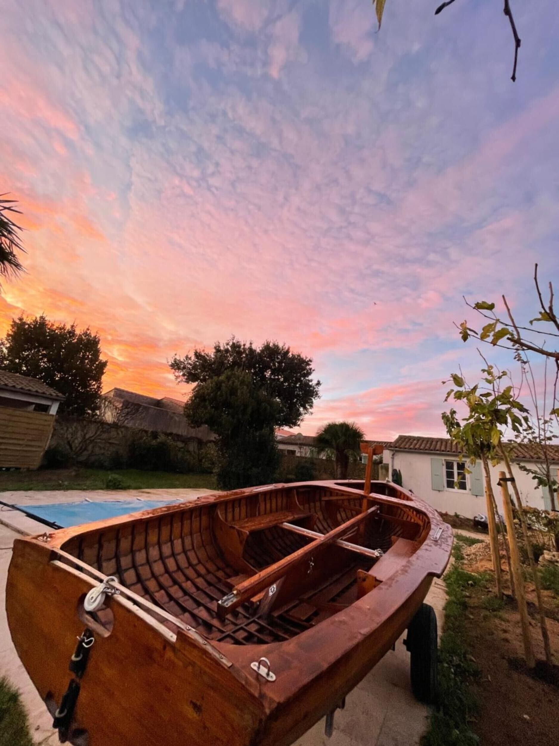 Un bote de madera en un patio trasero con piscina, árboles y una casa al fondo.