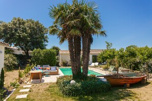 Un giardino sul retro con piscina, sedie a sdraio, una barca e una palma.