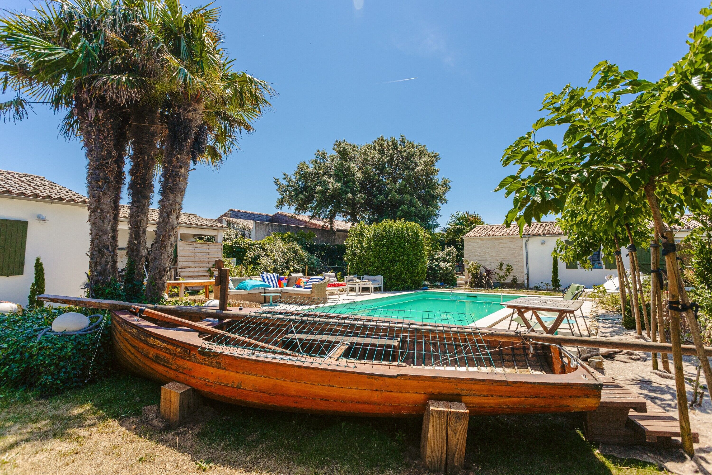 Zona de piscina con un bote de madera, palmeras y un cielo azul despejado.