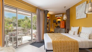Une chambre d’hôtel comprenant un lit, une porte-fenêtre coulissante donnant sur une terrasse, un petit coin salon et une kitchenette.