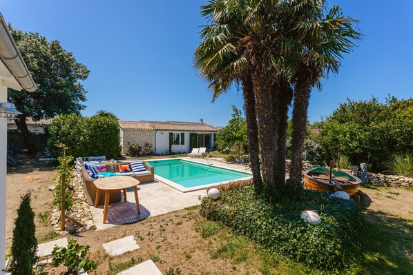 Un jardin avec une piscine, du mobilier d’extérieur, un palmier et un bateau.