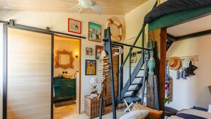 Una habitación con literas, una escalera, un baño con un lavamanos verde y varias decoraciones, incluyendo un flotador y fotografías enmarcadas.