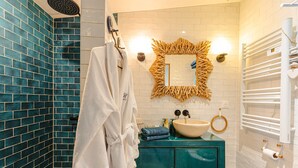 Un baño con ducha de azulejos azules, un albornoz blanco, un lavamanos con espejo de madera y un perchero para toallas.