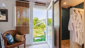 Un baño con ducha, una silla de mimbre con cojines y vistas al exterior.