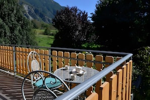 Un balcón con una mesa dispuesta para té, sillas y vistas a un paisaje montañoso.