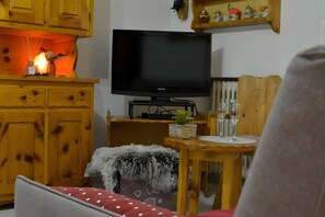 Una sala de estar con televisor, armarios de madera, un sofá rojo y una mesa de comedor con vasos.
