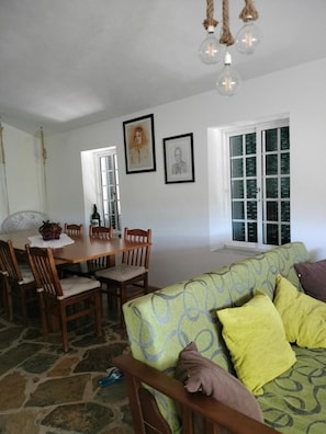 A dining area with a wooden table and chairs, a green sofa with patterned cushions, and two framed artworks on the wall. - Country House 'Casa De Canelas - Refugio Terroir' with Mountain View, Wi-Fi and Air Conditioning (Açoreira)