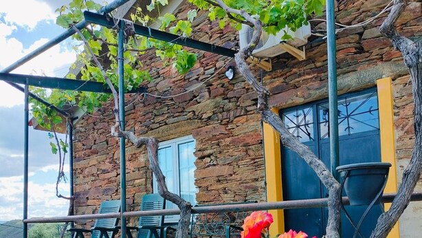 Un rustico edificio in pietra con una pergola, posti a sedere all'aperto e vista sulla campagna.