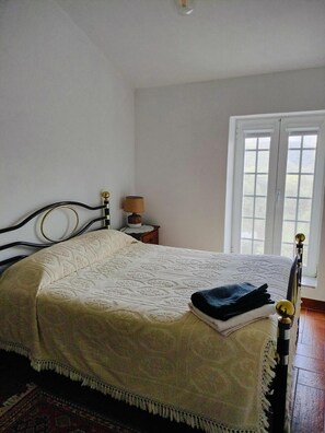 A bedroom with a bed, a nightstand, a lamp, and a window. - Country House 'Casa De Canelas - Refugio Terroir' with Mountain View, Wi-Fi and Air Conditioning (Açoreira)