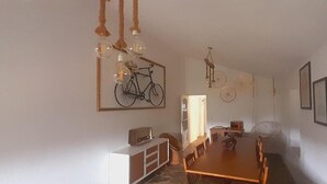 Zona pranzo con tavolo e sedie in legno, un armadietto bianco e un'opera d'arte raffigurante una bicicletta al muro.