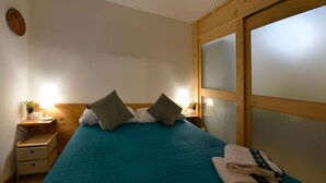 Quarto com cama, almofadas, mesa de cabeceira, luminária e janela com vidro fosco.