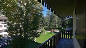 Uma varanda com vista para um gramado bem cuidado, uma árvore e um prédio ao longe.