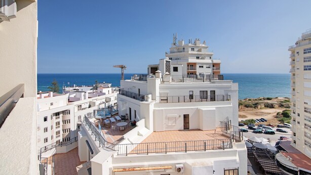 A multi-story building with a rooftop terrace, a view of the sea, and a parking area.