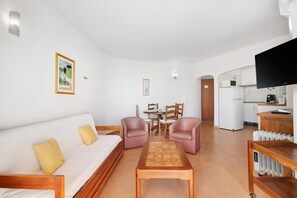 A living room with a sofa, two armchairs, a coffee table, a dining table with chairs, a kitchen area with a refrigerator, microwave, and a TV. - Colmeia AL - Casa Pólen (Armação de Pêra)