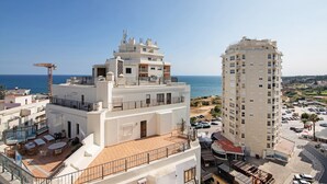 A multi-story building with a rooftop terrace, a pool, and a view of the sea.