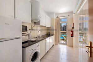 A modern kitchen with a washing machine, a refrigerator, and a window overlooking a pool.